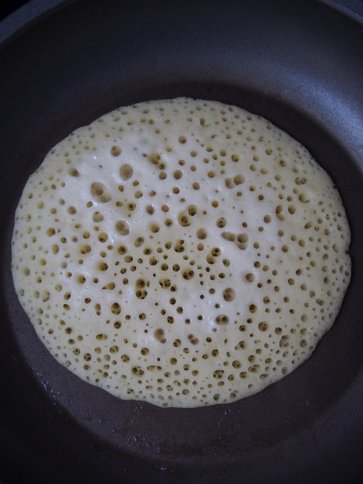 cooking baghrir, Moroccan semolina pancakes towards end of cooking pancake with batter almost dry on top.