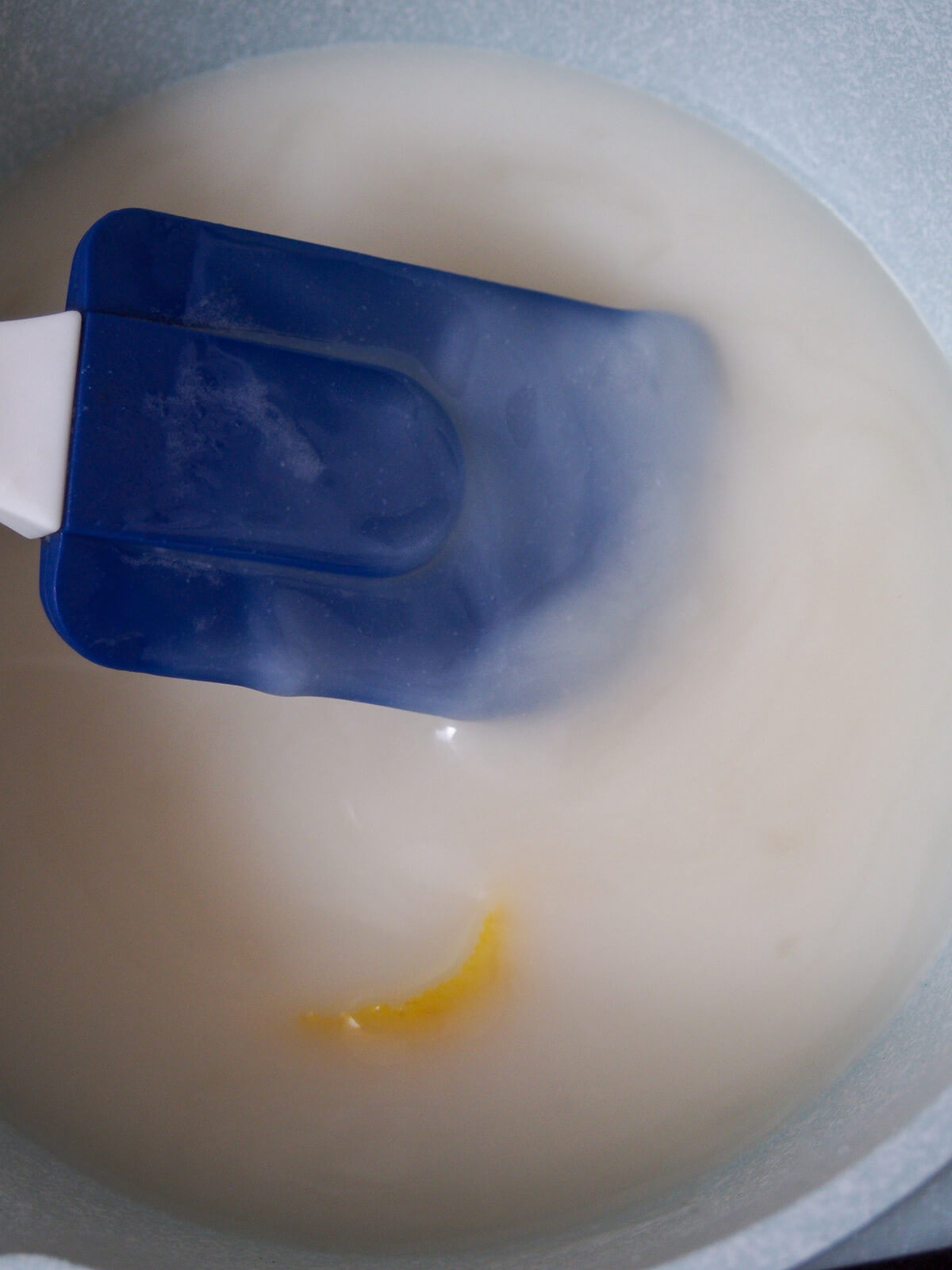 stirring menjarblanc, almond pudding, with spatula as it thickens in pan.