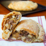 close view of Cornish pasty in half with one half on top of other on kitchen towel.