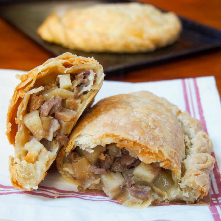 close view of Cornish pasty in half with one half on top of other on kitchen towel.