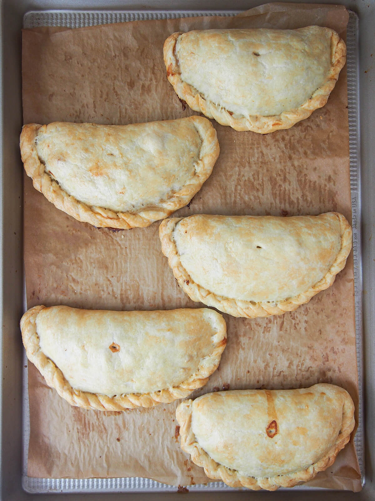 baking sheet with five Cornish pasties on top, fresh out the oven, from overhead.