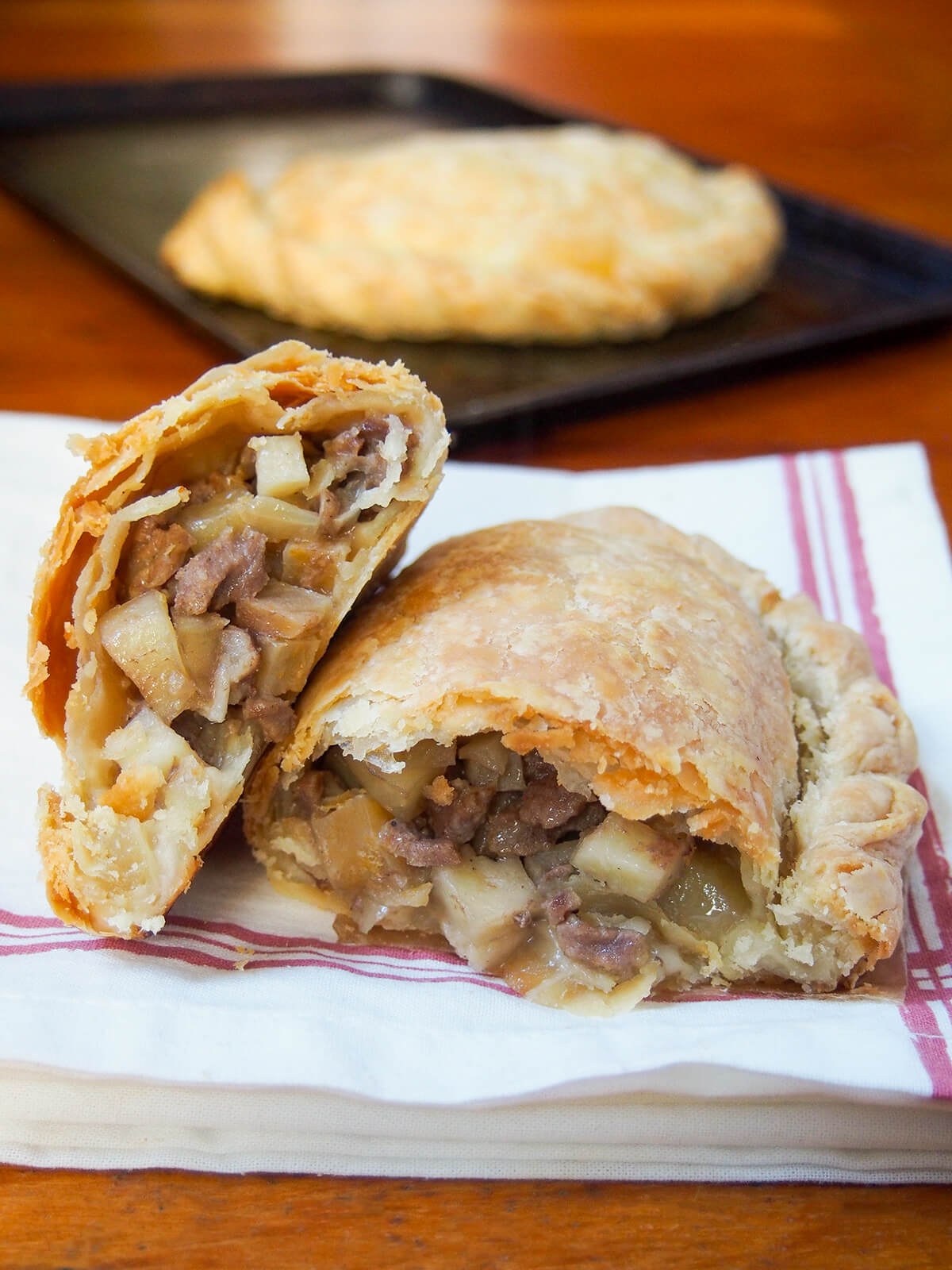 split open Cornish pasty with one half resting on other side on a white kitchen towl, whole pasty behind.