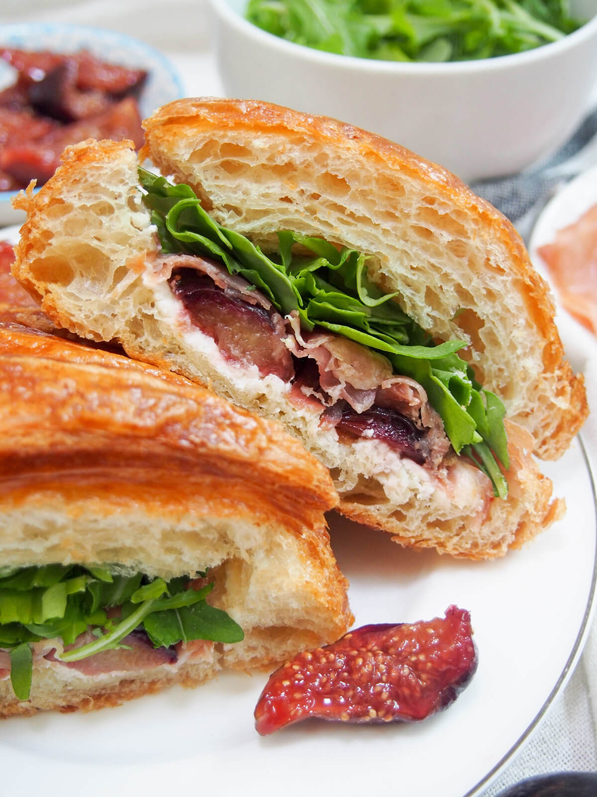 close view of half of prosciutto and goat cheese croissant sandwich showing the figs, ham and arugula filling.