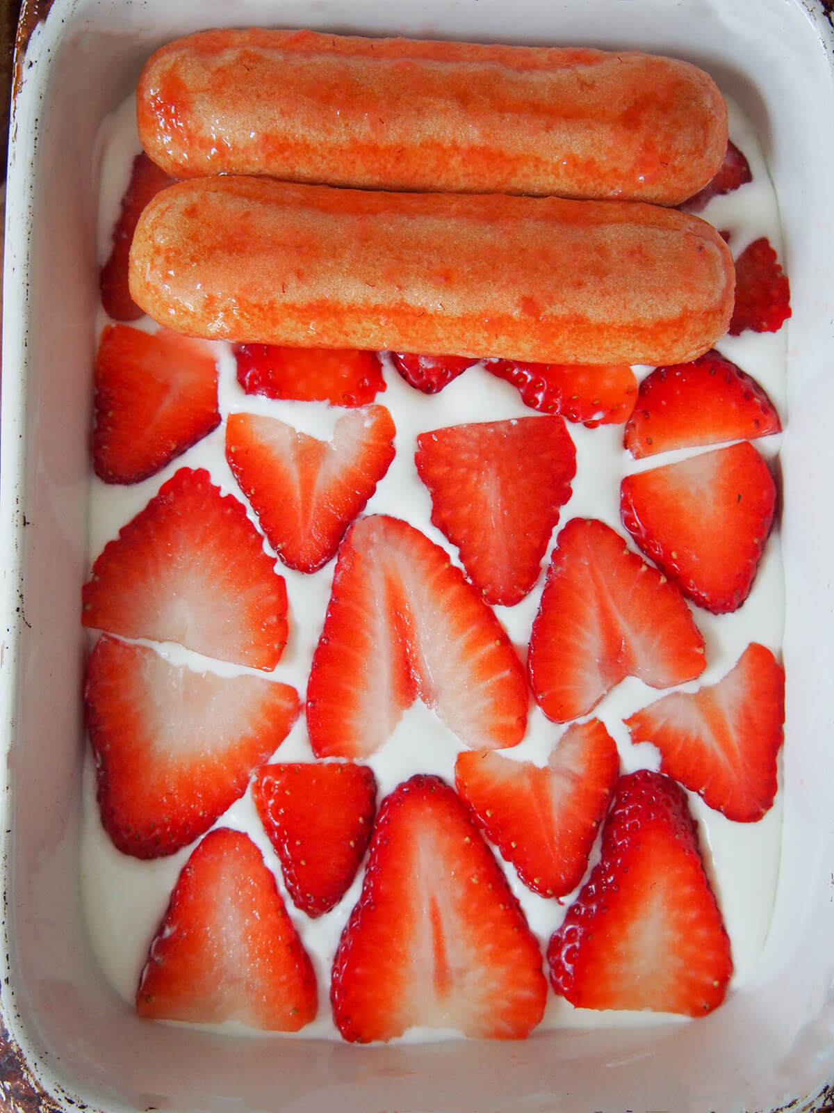 adding second layer of dipped cookies on top of cream and strawberry slices layers.