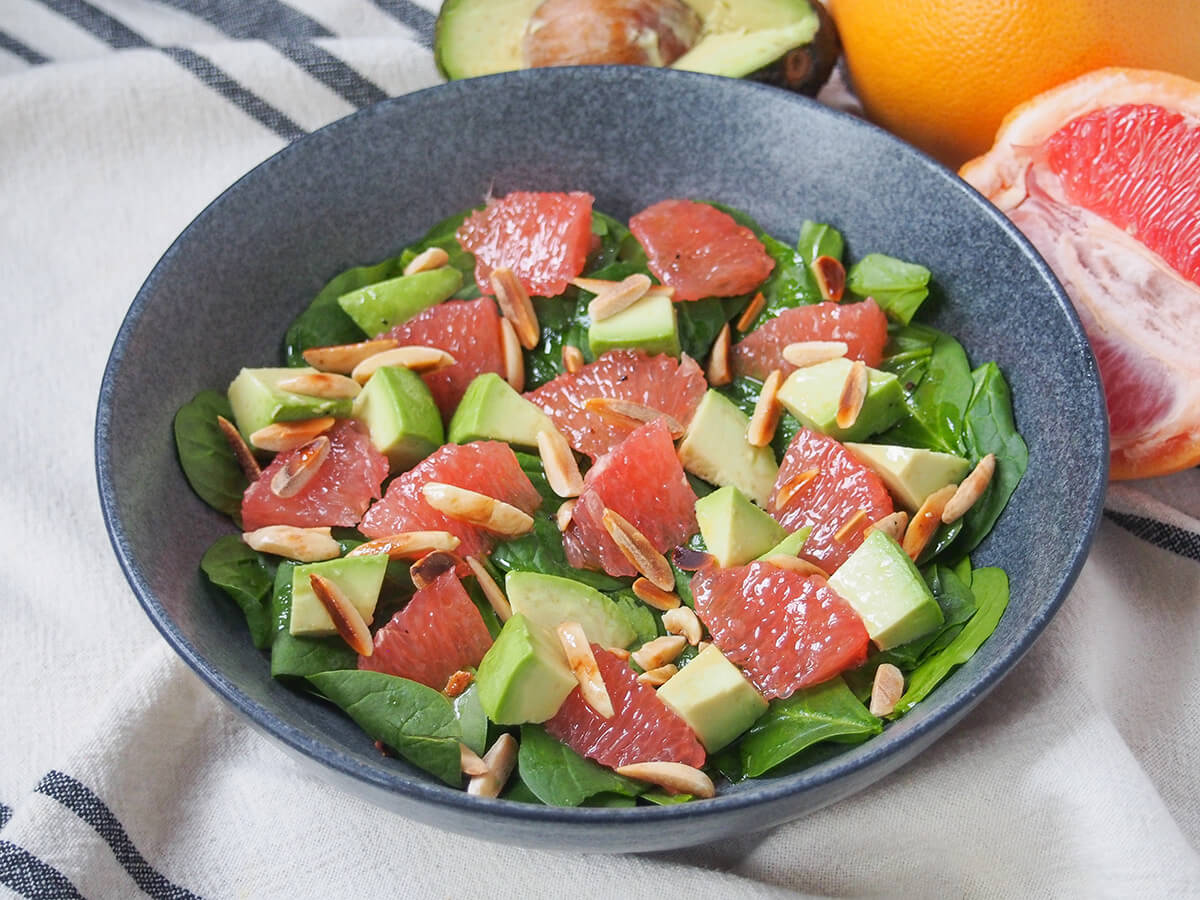 side view of bowl of avocado grapefruit salad with part grapefruit and avocado in the background.