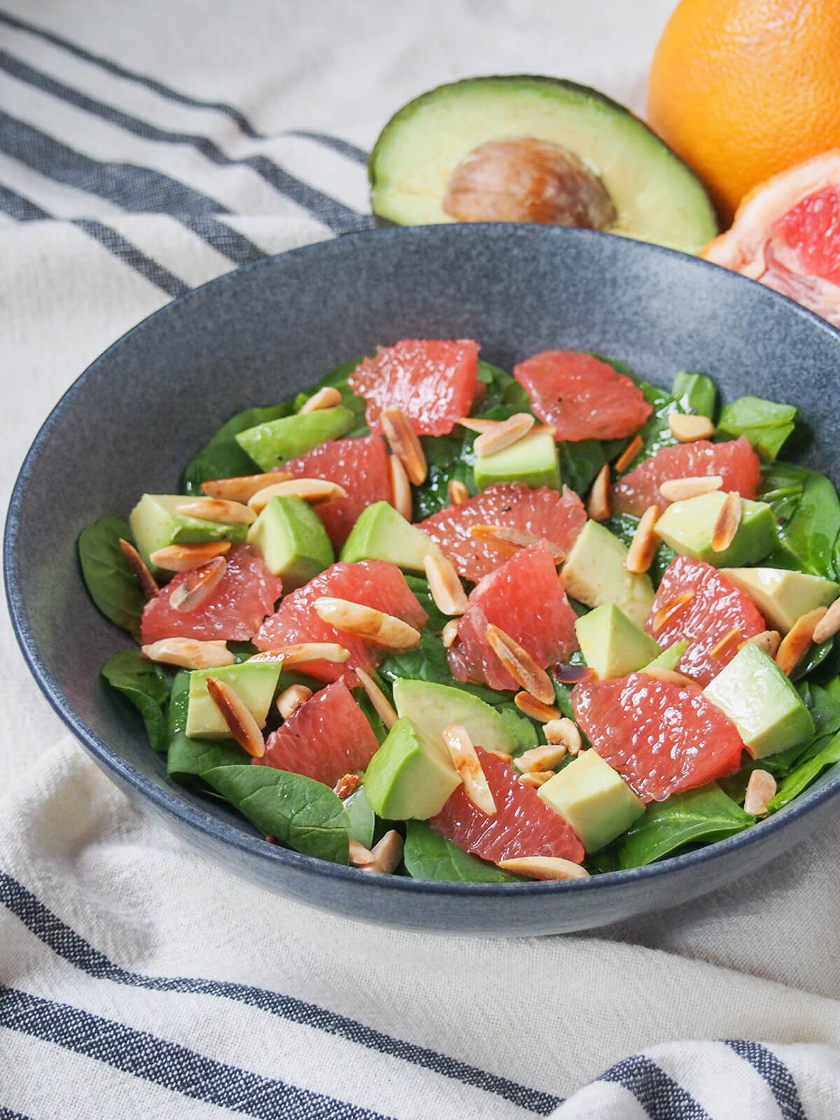 side view of bowl of avocado grapefruit salad with avocado and grapefruit behind.