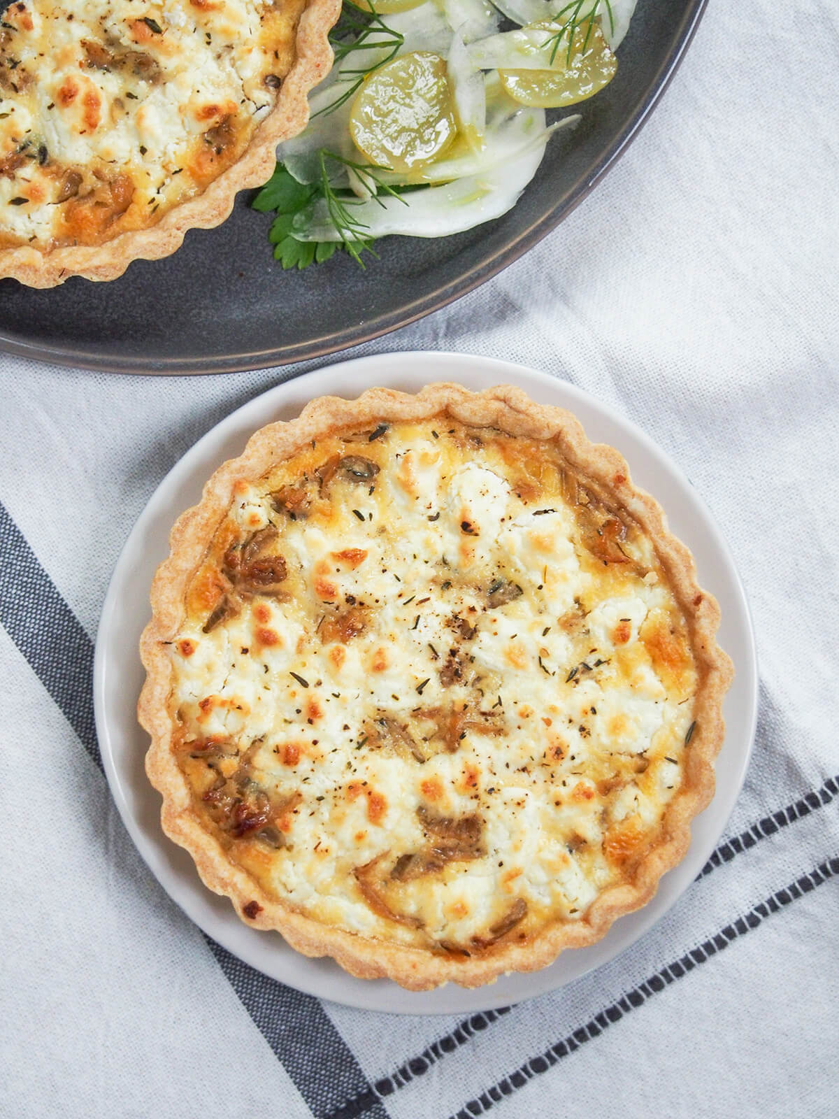 overhead view of caramelized onion and goat cheese tart on plate with part of another above.
