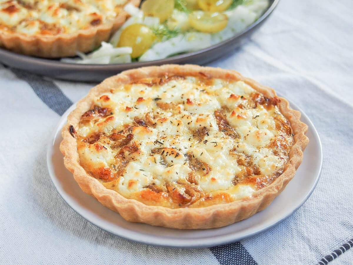 side view of a caramelized onion and goat cheese tart with another and salad on plate behind.