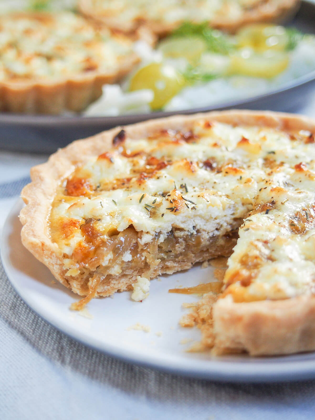 caramelized onion and goat cheese tart with a slice taken out showing onion layer below cheese in filling.