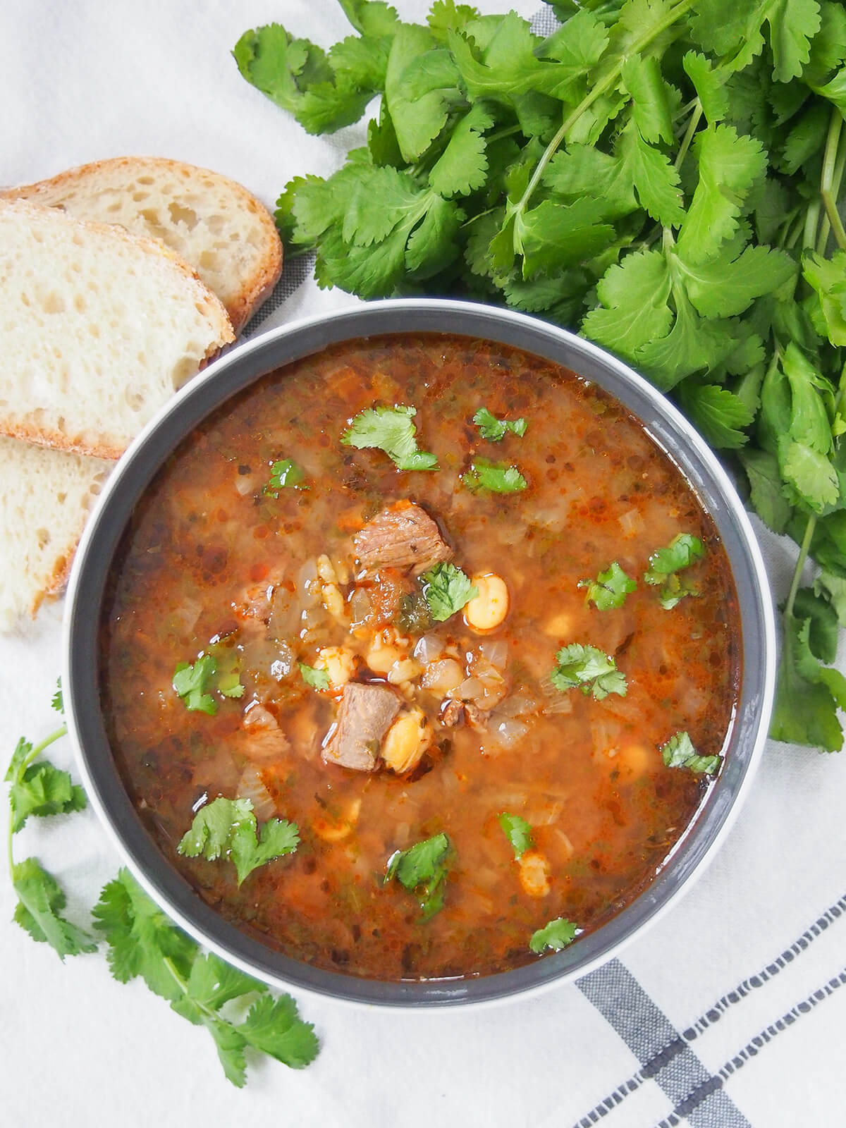 bowl of chorba frik with cilantro bunch and bread beside bowl, from overhead.