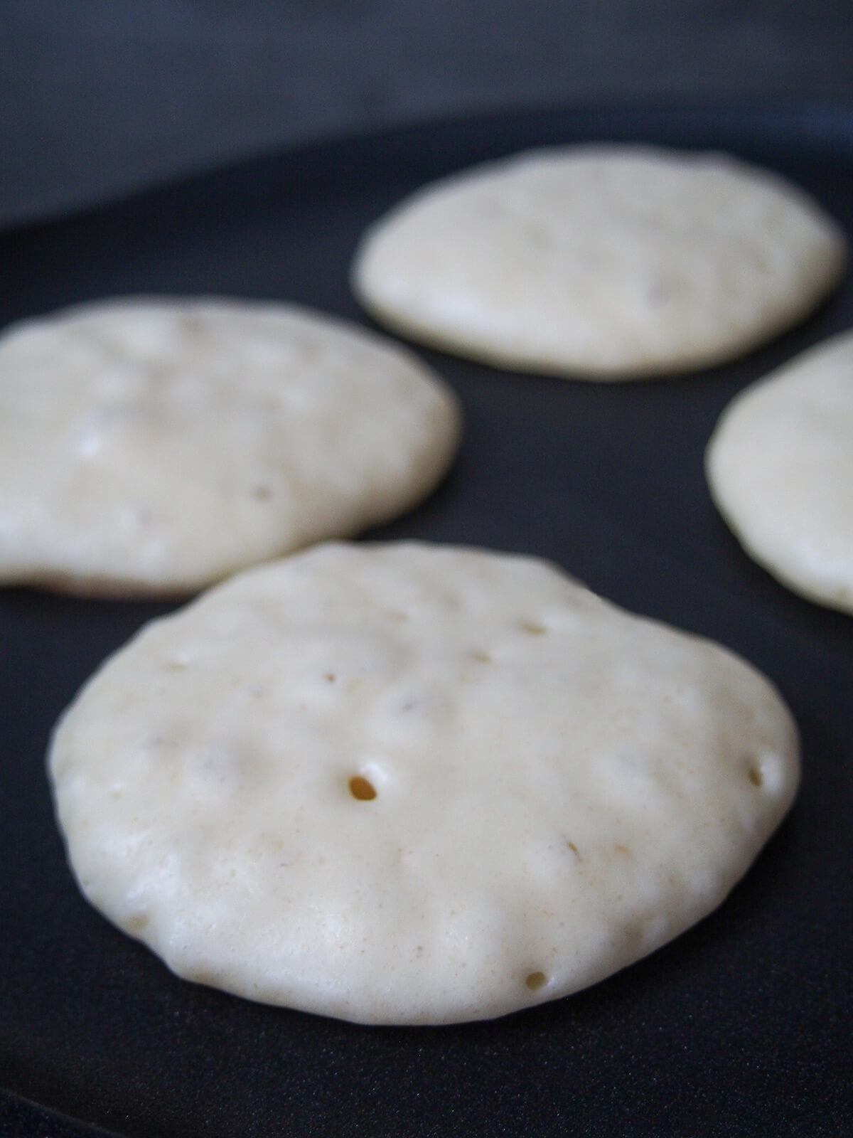 cooking pancakes on griddle with bubbles forming on top surface.