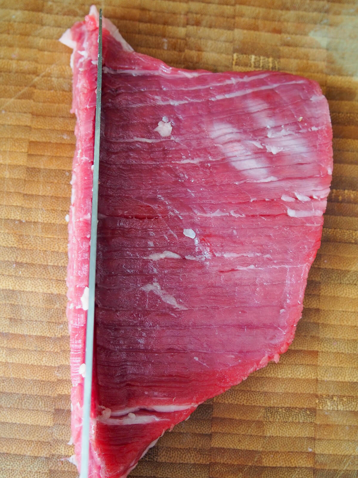 knife over piece of flank steak about to cut slice, across the grain.