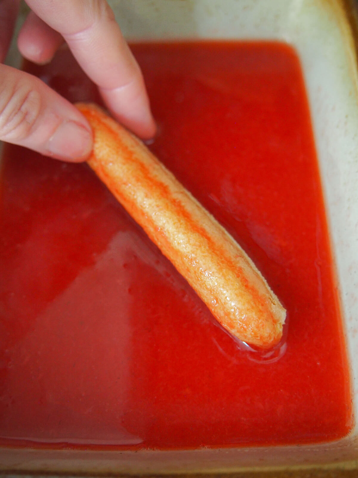 dipping a ladyfinger cookie in strawberry syrup