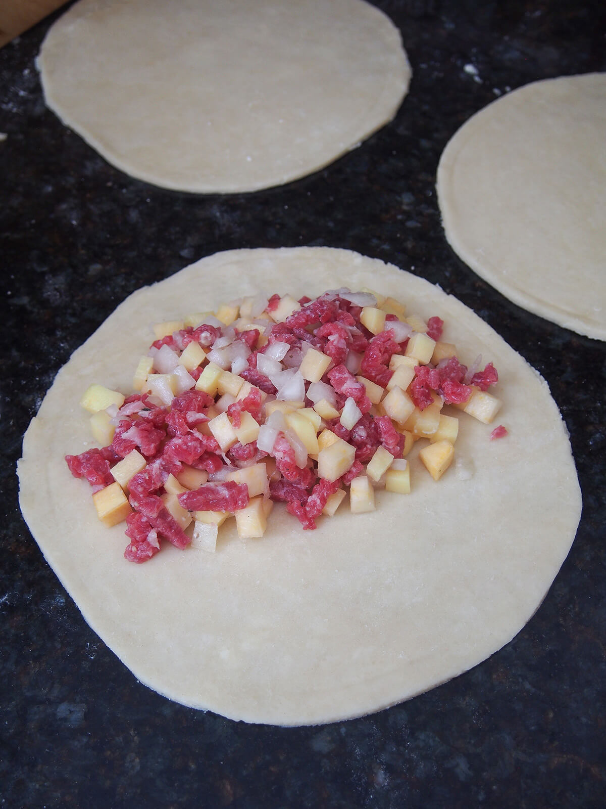 cut circles of pastry with meat and vegetable filling on front piece on one side.