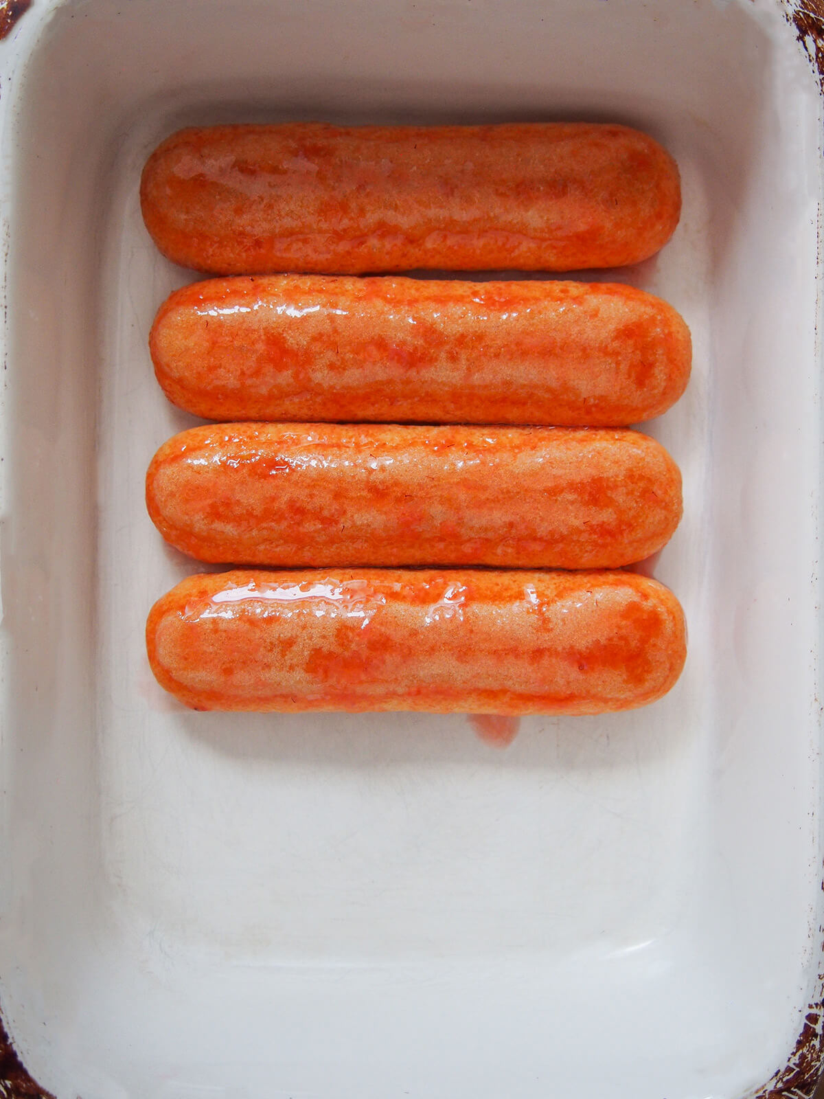 four syrup dipped ladyfinger cookies in a row in a dish from overhead.