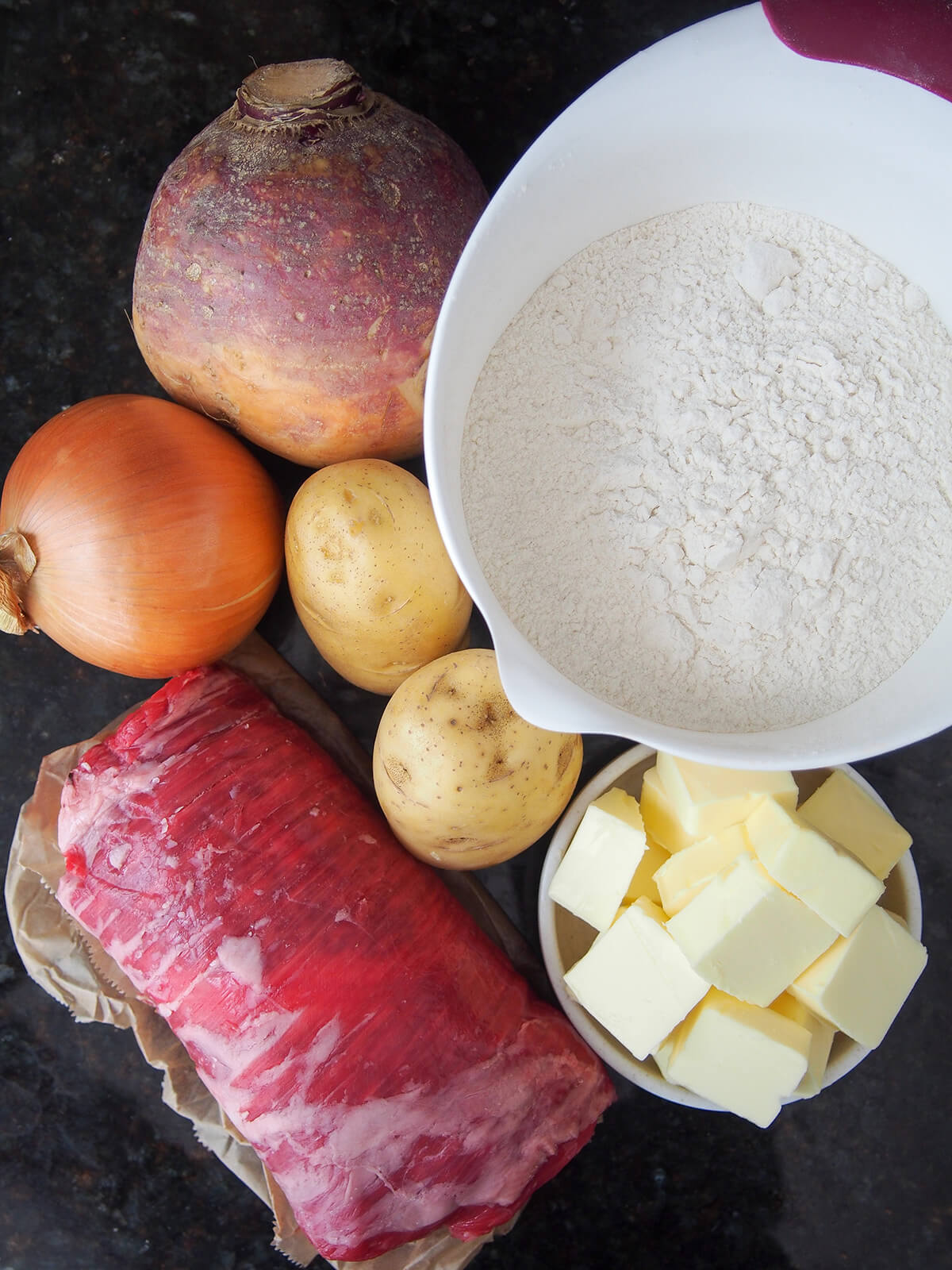bowl of flour, diced butter in small dish with potatoes, rutabaga, onion and skirt steak to side.