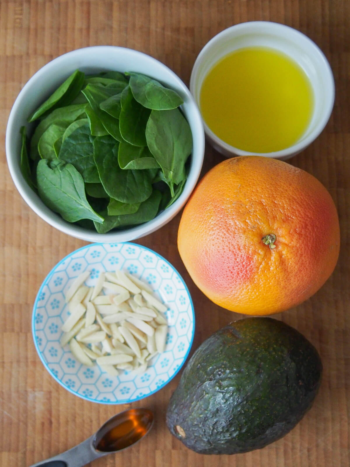 bowl of spinach, olive oil, almond slices, with avocado, grapefruit next to them.