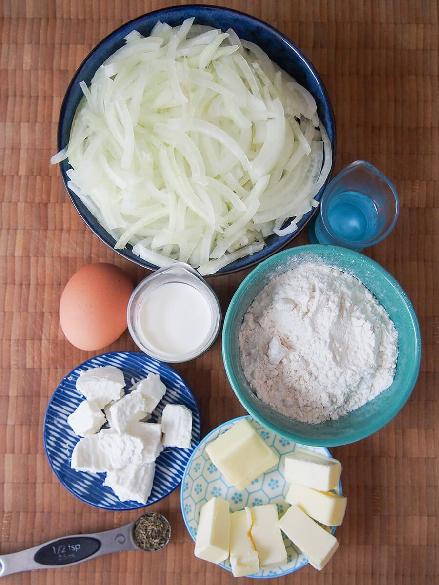 bowls with sliced onions, flour, butter, goat cheese and egg and milk measures to side.