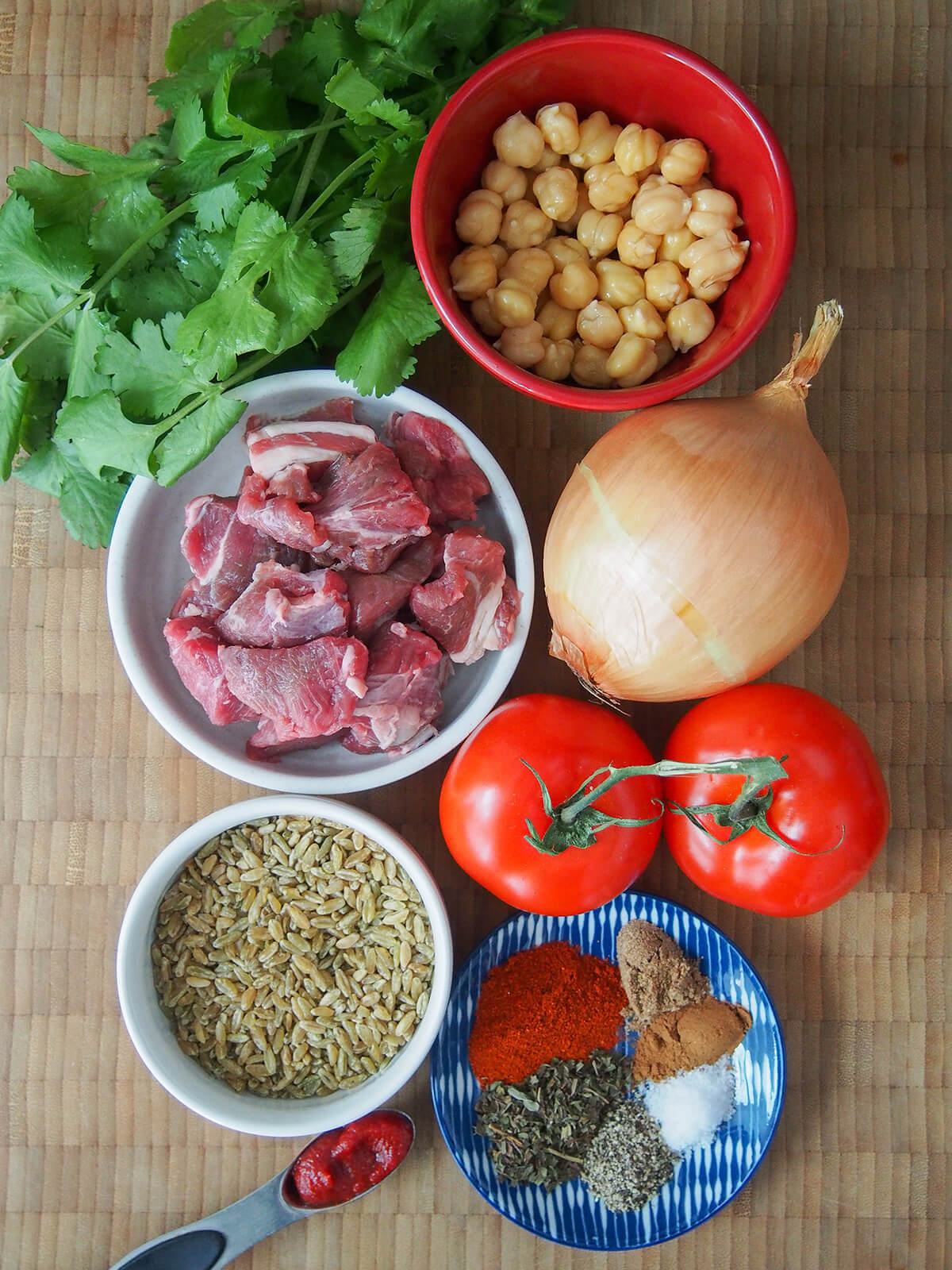 bowls of lamb, chickpeas, freekeh, spices and tomatoes, onion and cilantro bunch around bowls.