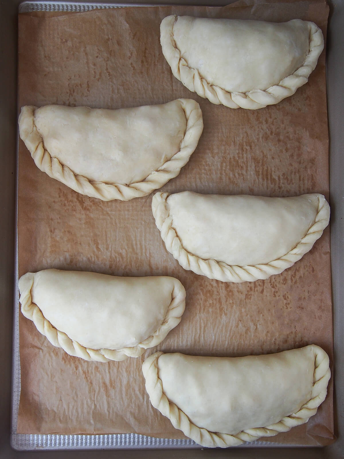 formed but uncooked Cornish pasties on lined baking sheet viewed from overhead.
