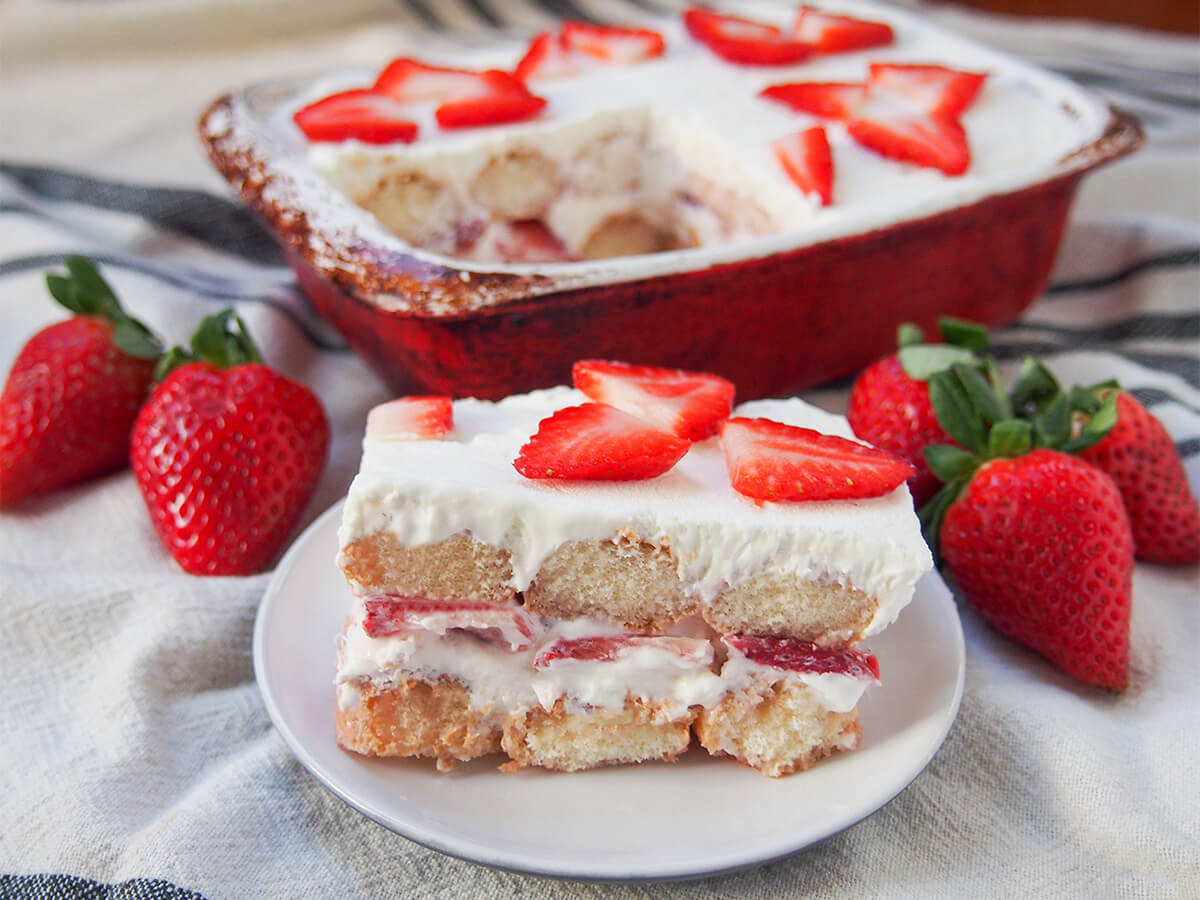 slice of strawberry tiramisu in front of dish with more and strawberries to either side.