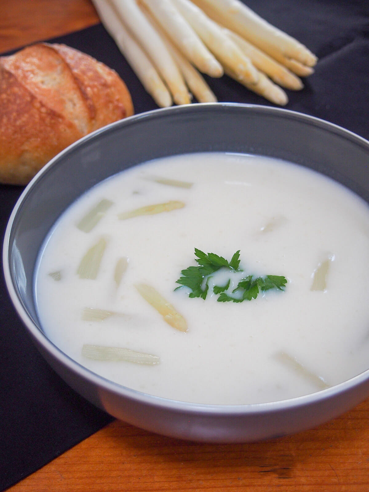 side view of bowl of white asparagus soup with white asparagus bunch behind.