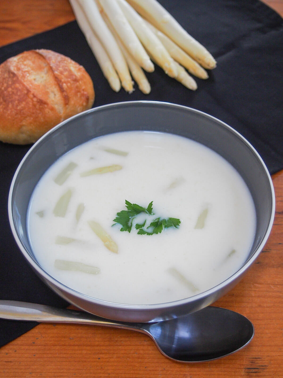 bowl of white asparagus soup with asparagus and roll behind.