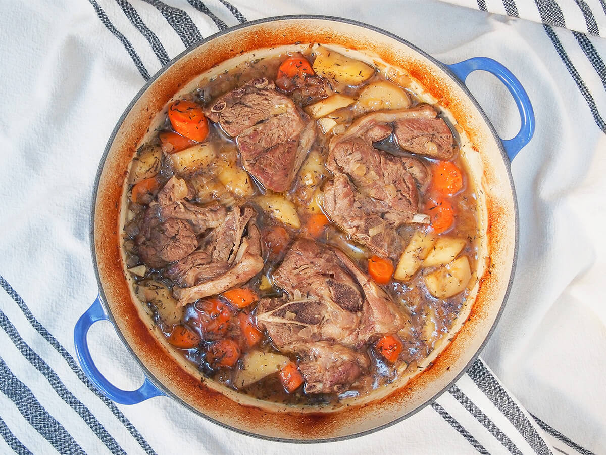 overhead view of braised lamb shoulder chops and vegetables in dish.