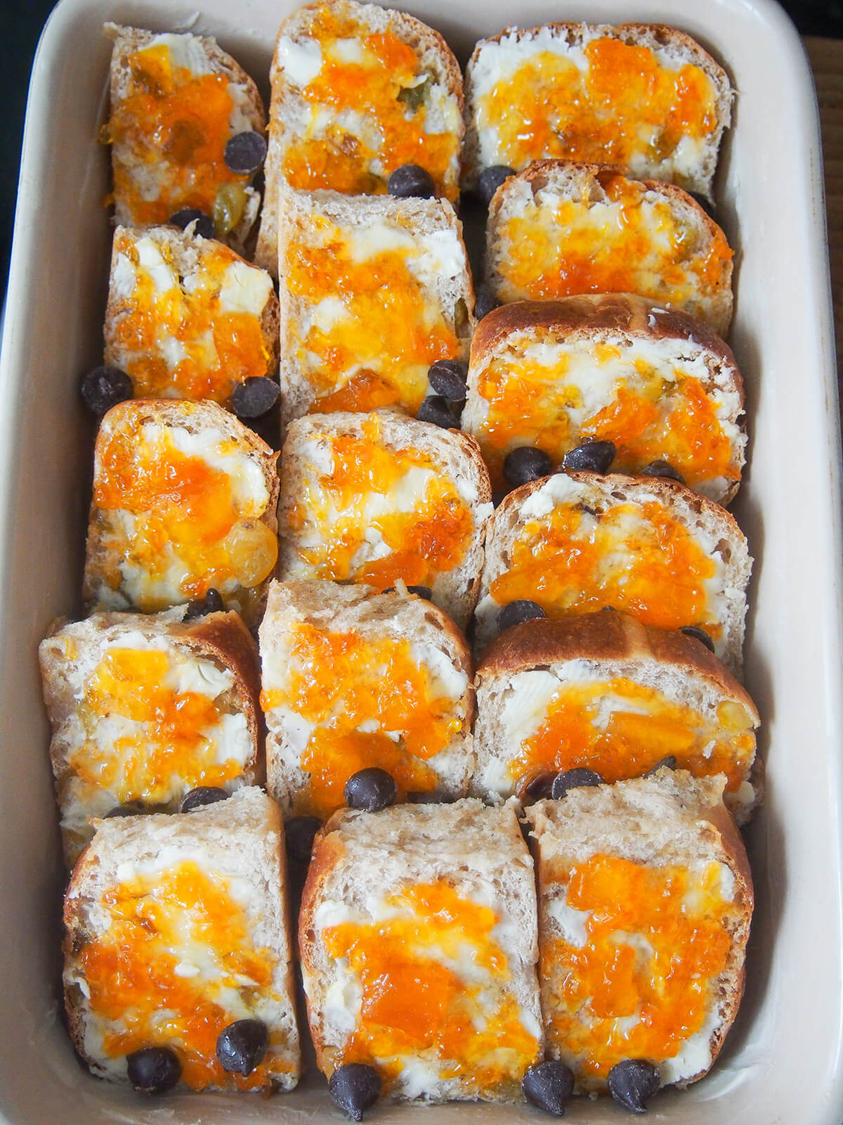 overlapping slices of hot cross bun topped with butter and marmalade in baking dish.