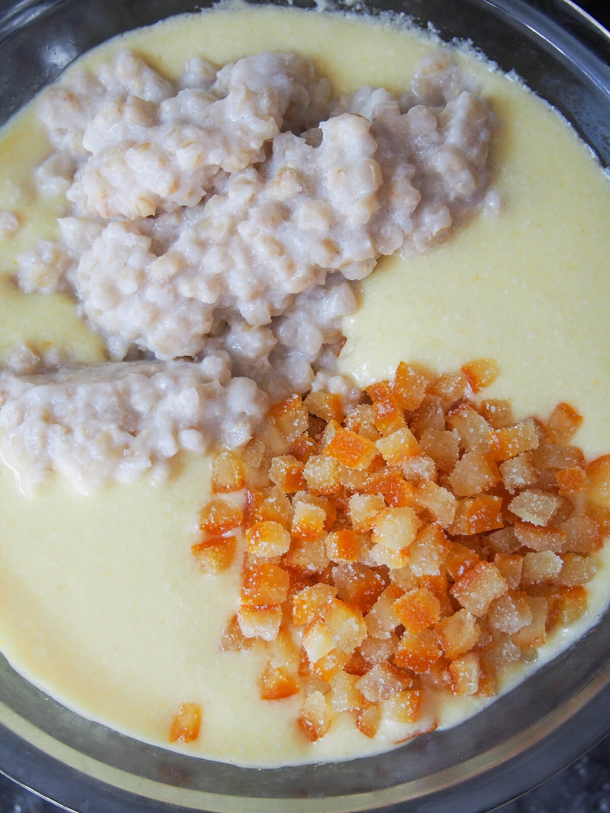 making filling for pastiera napoletana chopped candied orange peel and creamy cooked wheat in bowl with egg and ricotta mixture.