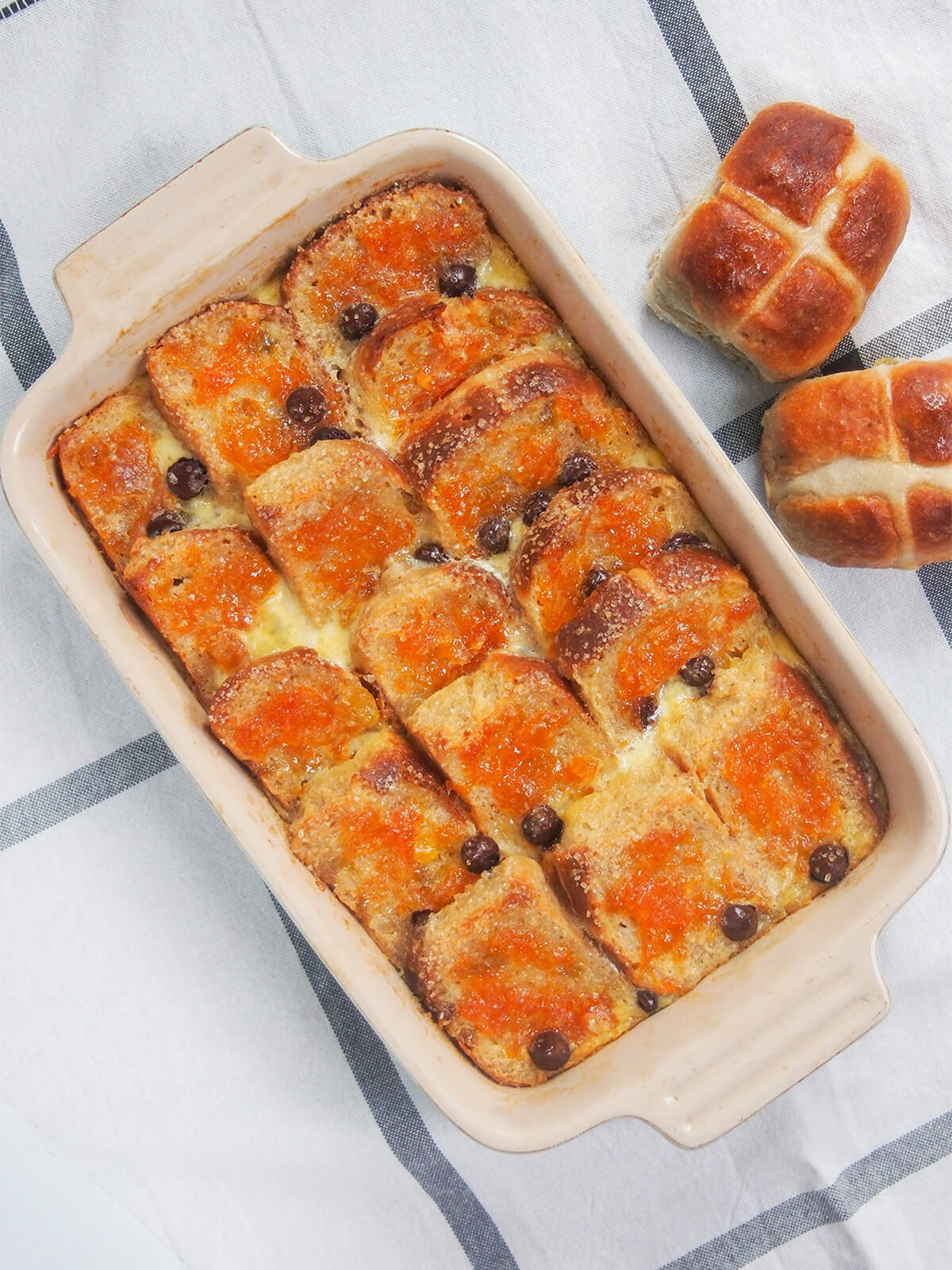 overhead view of a dish of hot cross bun bread and butter pudding with hot cross buns to side.