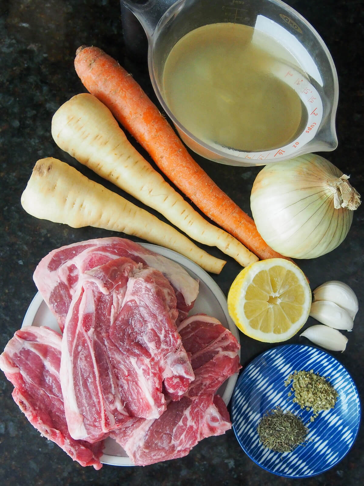 lamb shoulder chops, parsnips, carrot, onion, measure with stock, part lemon, garlic and small plate with dried herbs.