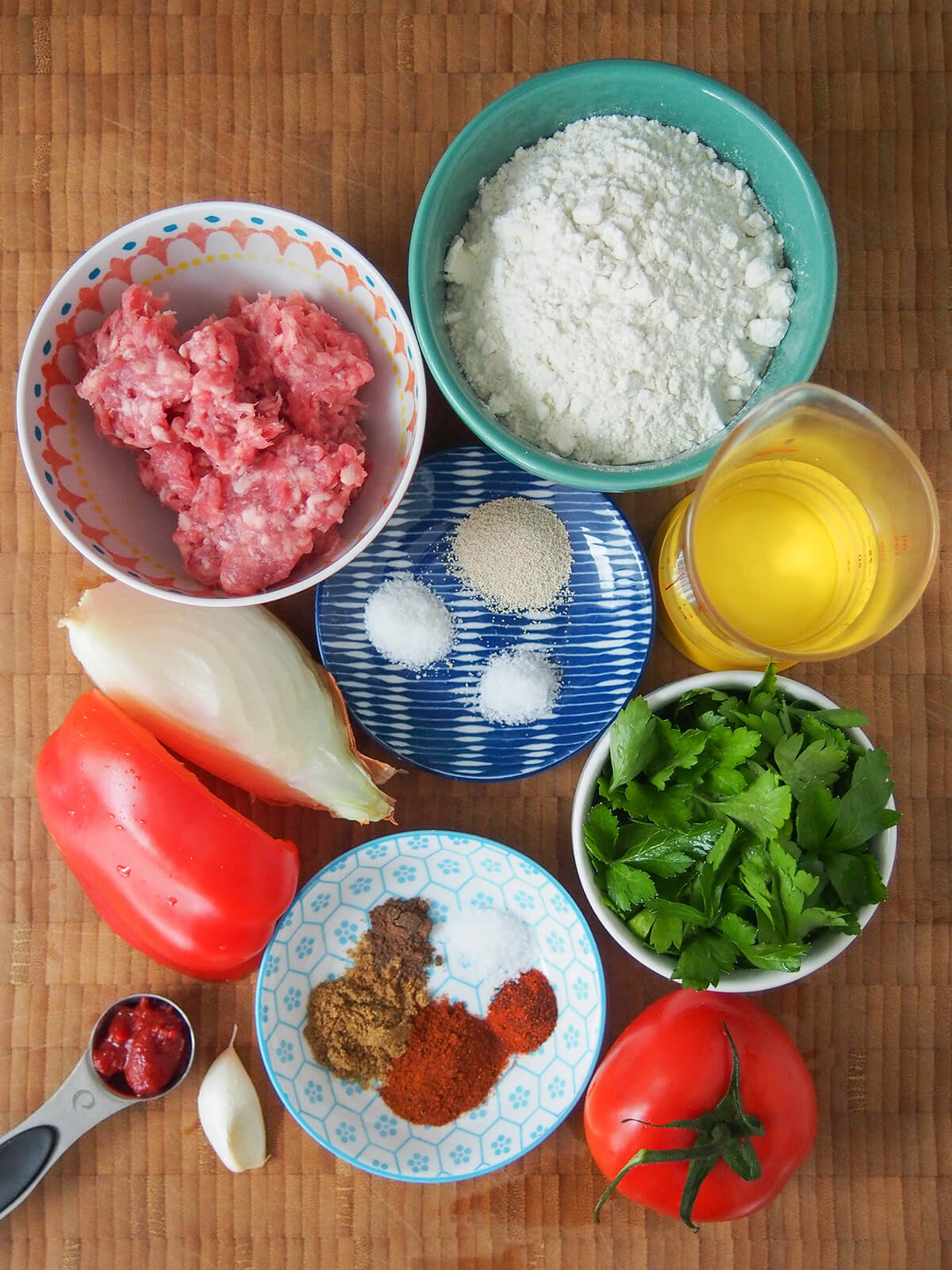 bowls with ground meat, flour, parsley, spices, yeast and salt with tomato, part pepper and onion plus glarlic clove around.