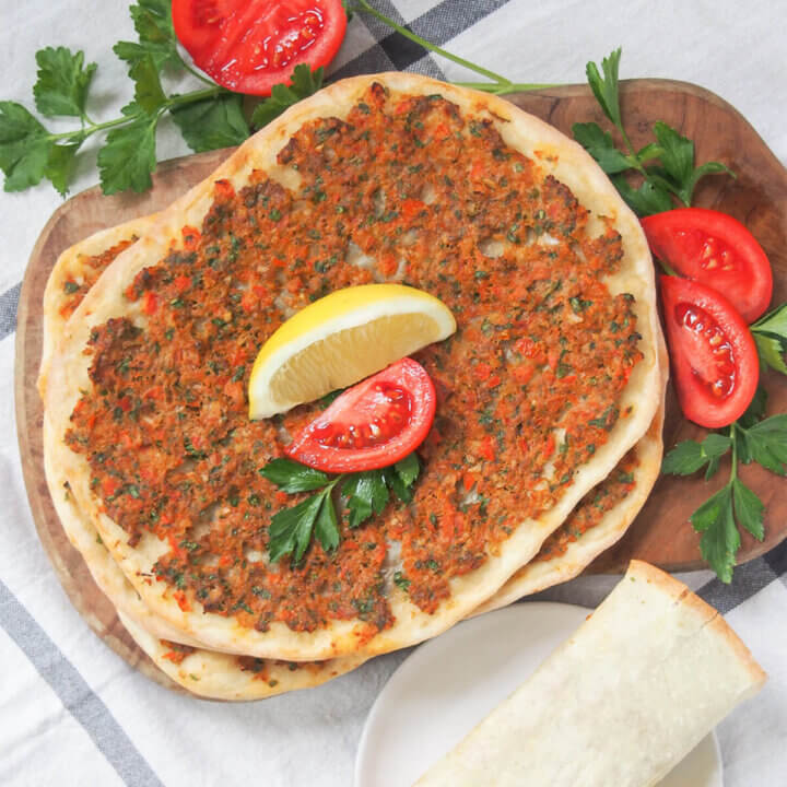 lahmacun Turkish pizza with tomato slice and lemon wedge on top.