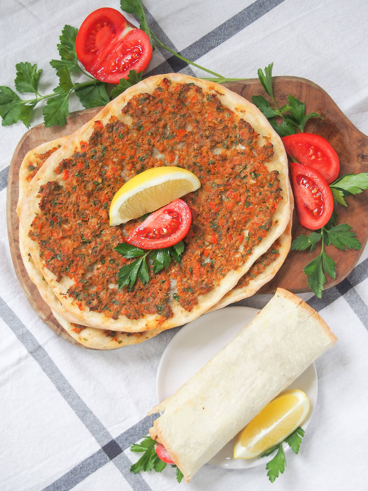 overhead view of lahmacun Turkish pizza with tomato to side and a rolled pizza on plate below.