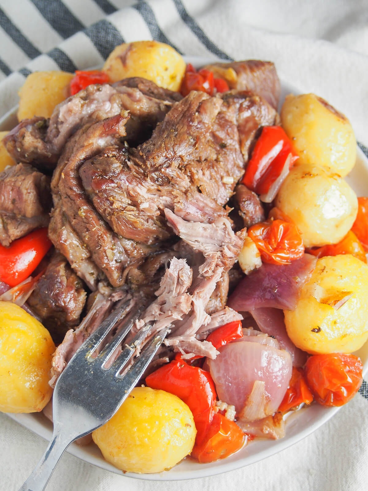 Lamb kleftiko is a classic Greek dish for good reason. It takes a little time, but it's hands off cooking and is easy to make. A delicious Mediterranean meal. fork breaking up piece of the lamb with potatoes and other vegetables around it.