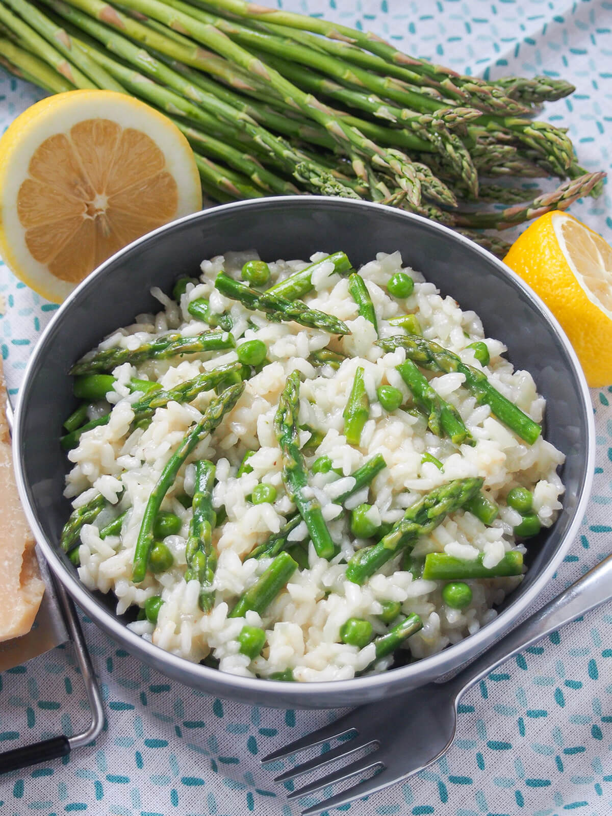 bowl of lemon asparagus risotto with bunch of asparagus and cut lemon behind bowl and fork in front.