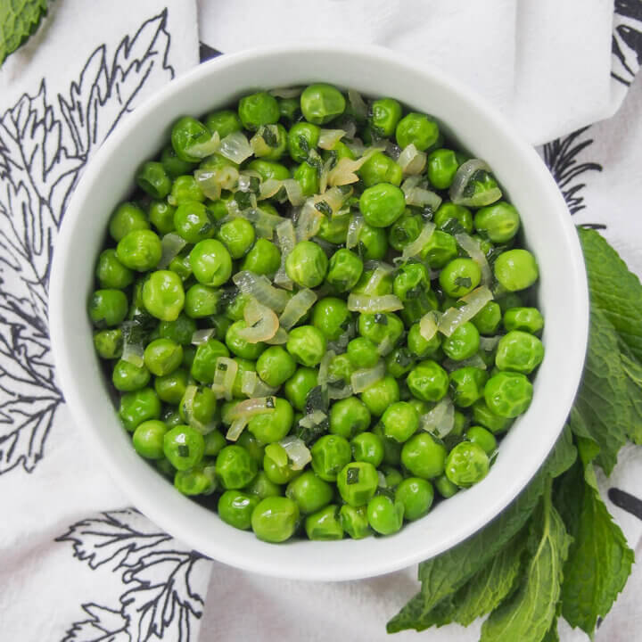 overhead view of a bowl of minted peas with mint to side.