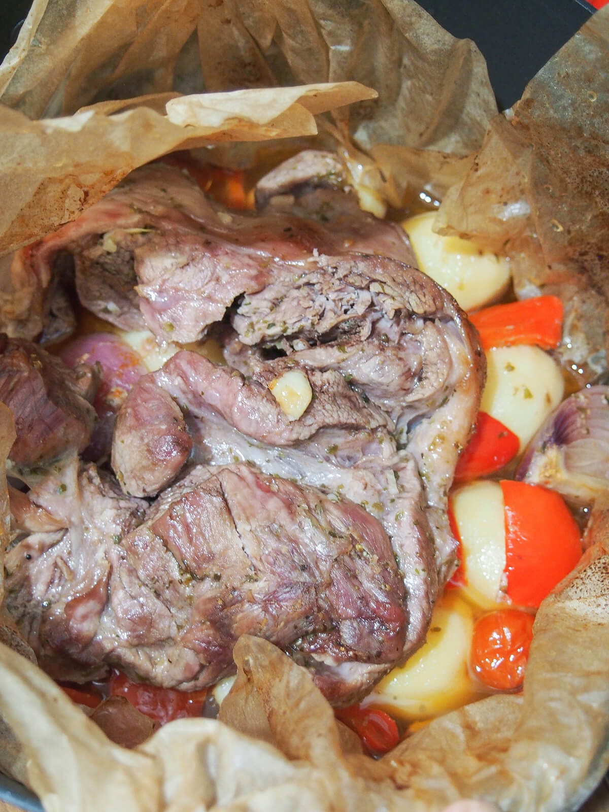 cooked lamb kleftiko open parchment after cooking showing lamb and vegetables underneath.