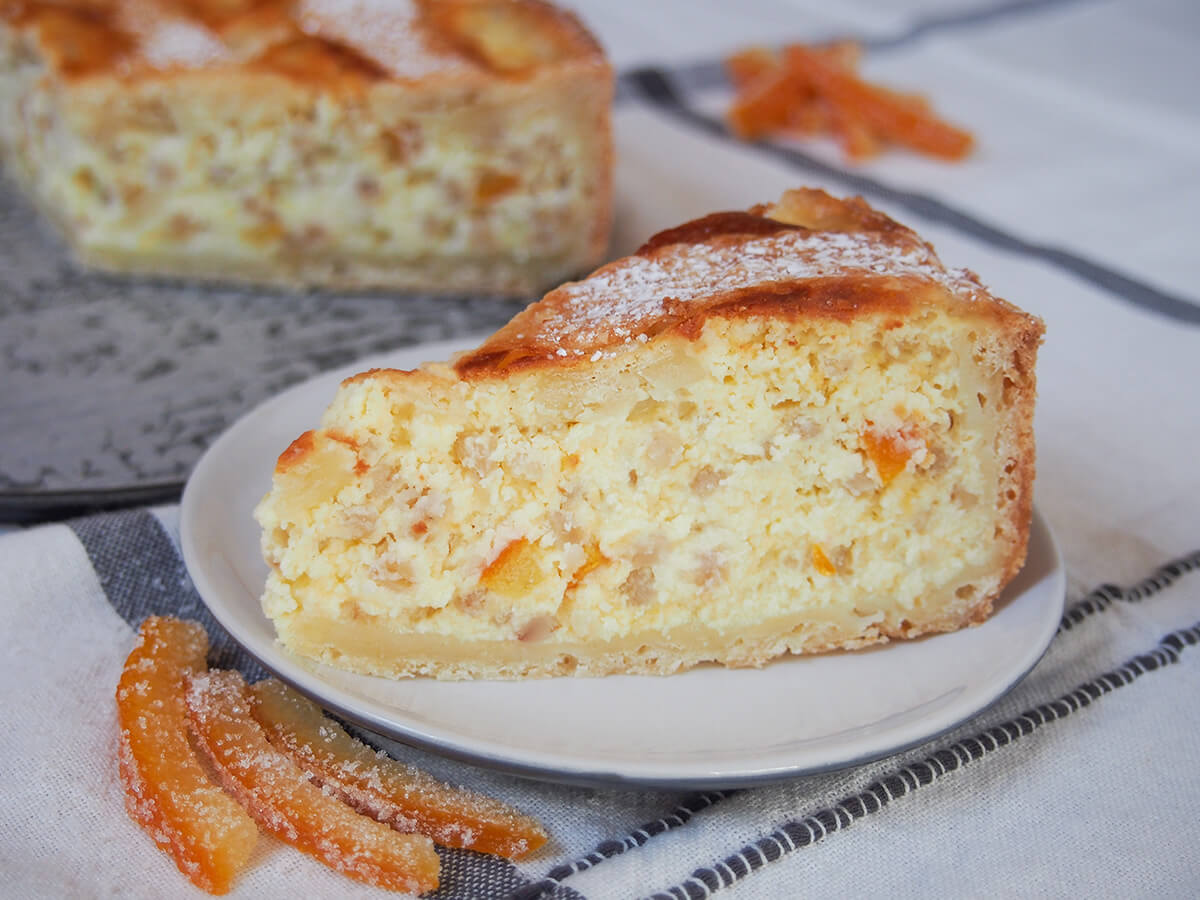 pastiera napoletana is a lovely Italian Easter dessert slice of pastiera napoletana on plate with pieces of candied orange peel below plate.