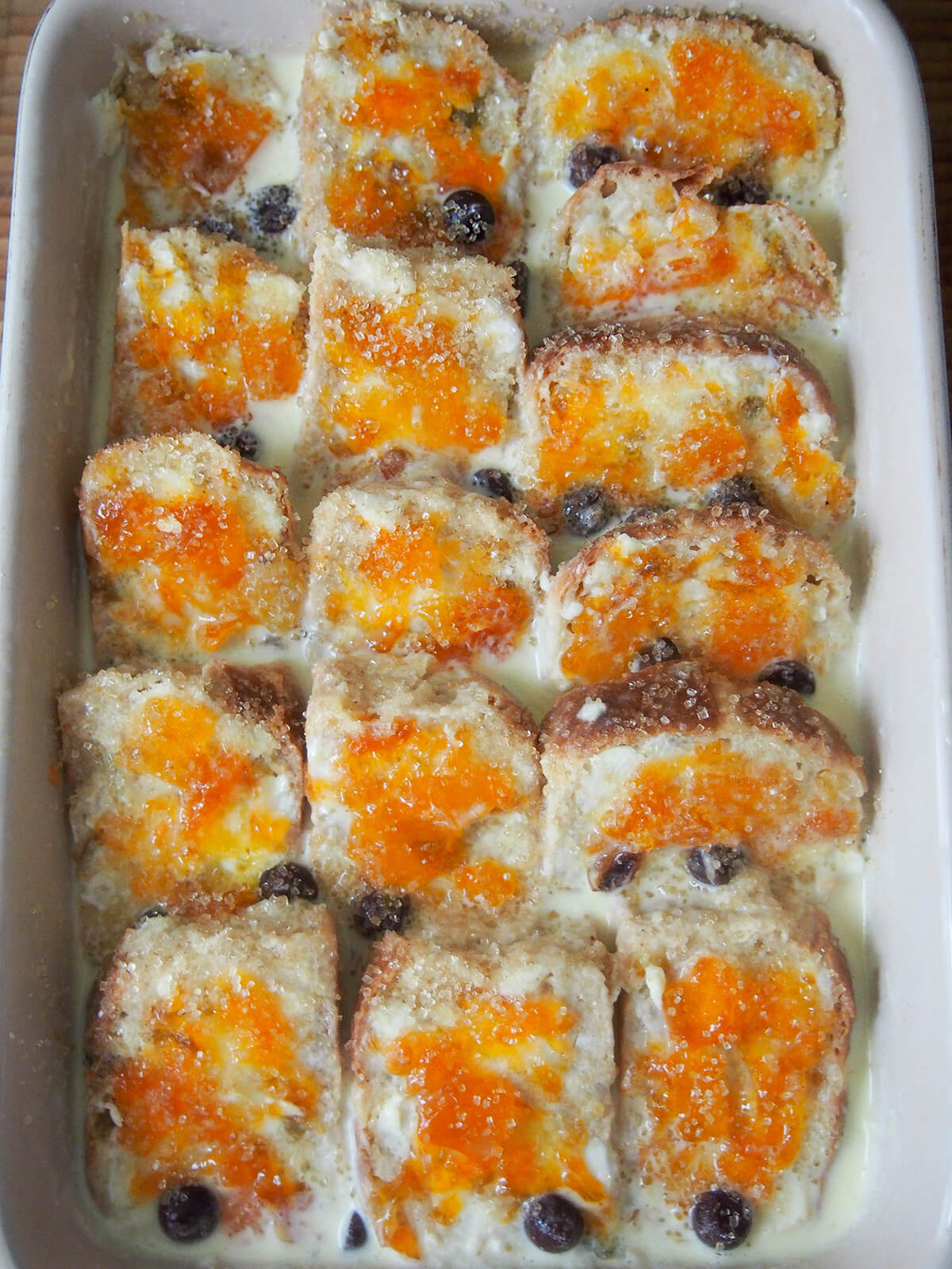slices of hot cross bun topped with butter and marmalade, soaked with custard mixture and with sugar over top before baking.