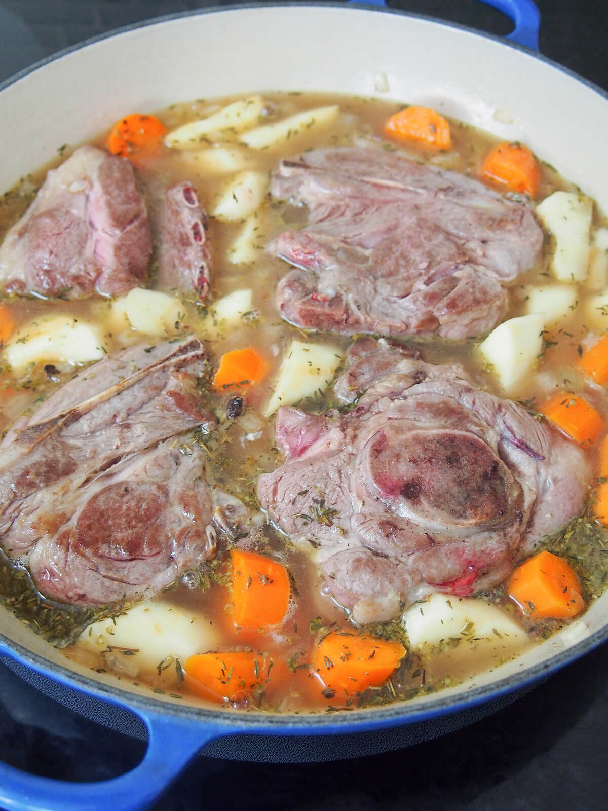 lamb shoulder chops, vegetables and stock in dish before cooking in oven.