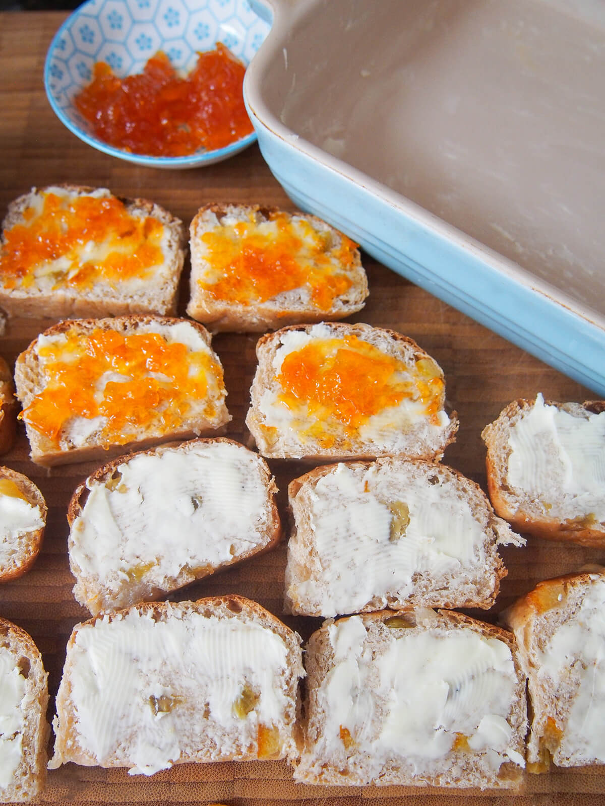slices of hot cross bun, some with butter and others also with marmalade on them, next to buttered baking dish