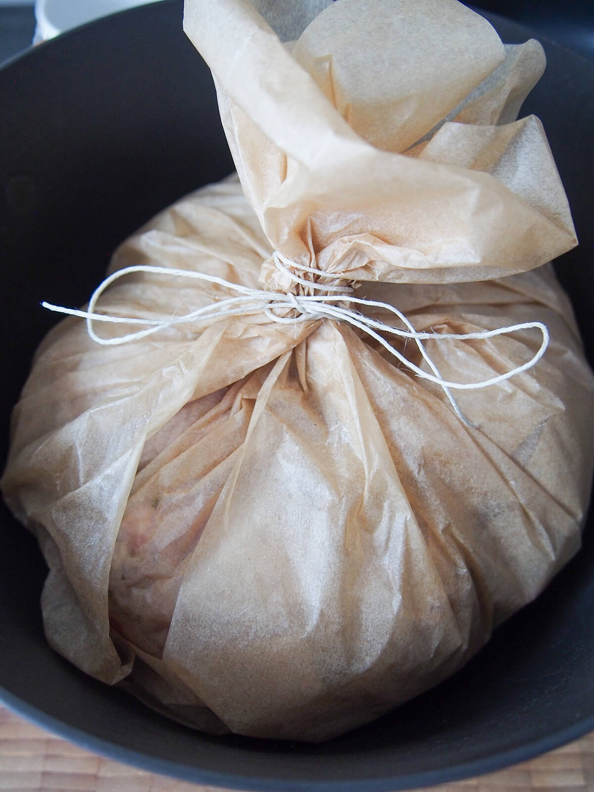 tied parchment containing lamb kleftiko bundle in parchment tied together with string inside a Dutch oven.