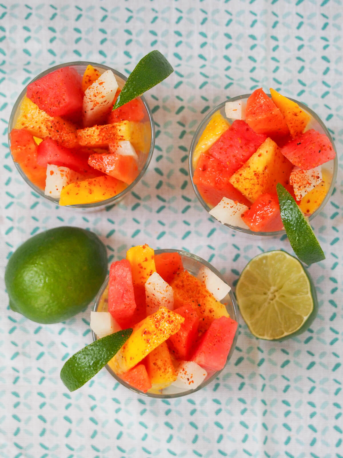 overhead view of three glasses of Mexican fruit cups with limes to side.