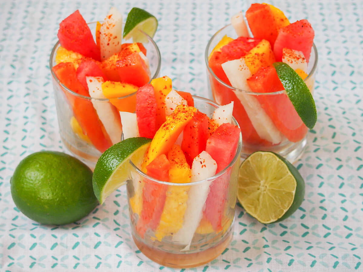three Mexican fruit cups from side with whole lime to one side, cut lime to other.
