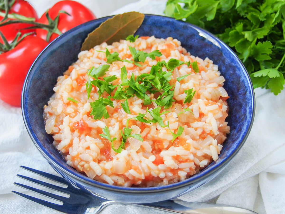 side view of Portuguese tomato rice in bowl with tomatoes and parsley behind.