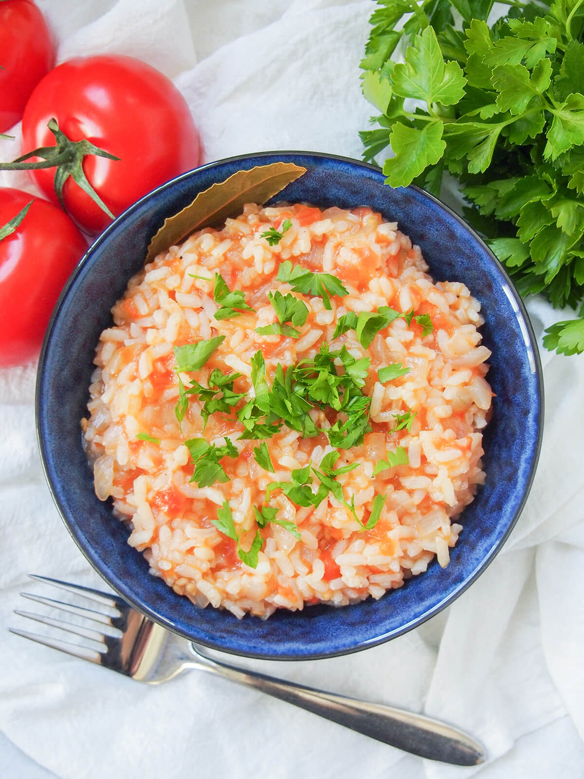 overhead view of bowl of Portuguese tomato rice with tomatoes and parsley above bowl and fork below.