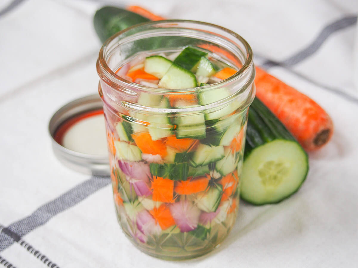 jar of acar timun jar of acar timun, Indonesian pickles from side with partial view of cucumber and carrot behind.