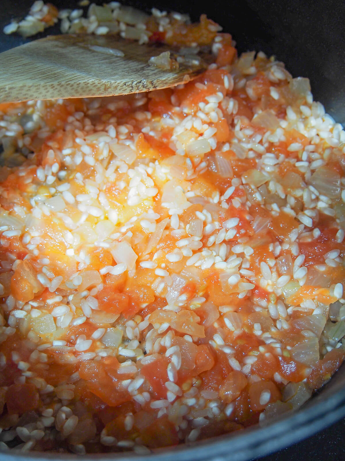 tomato, rice and onion in pot with wooden spoon at top.